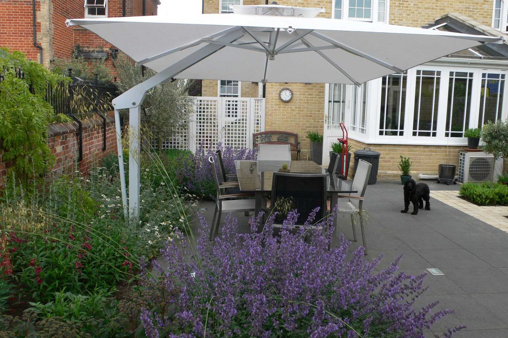 eating and seating area to complete the outdoor cooking experience. Large dining table and chairs shaded by a garden umbrella and surrounded by beautiful planting