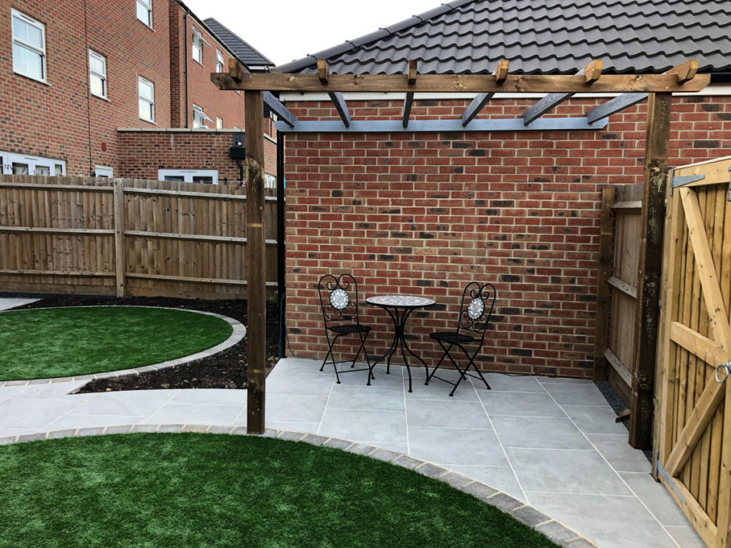 timber pergola beside a garage with porcelain patio and artificial grass