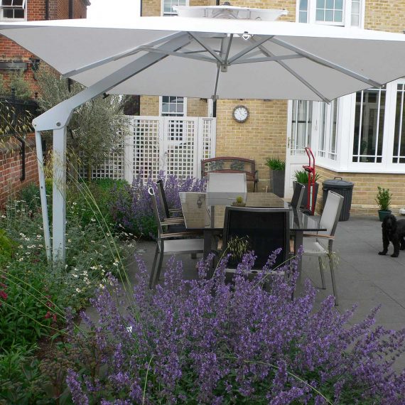 eating and seating area to complete the outdoor cooking experience. Large dining table and chairs shaded by a garden umbrella and surrounded by beautiful planting