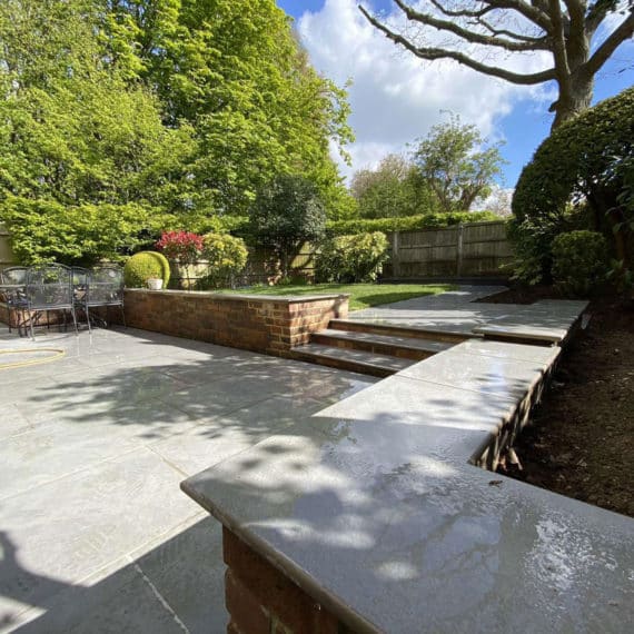 Attractive patio in mid sized garden with trees in the background