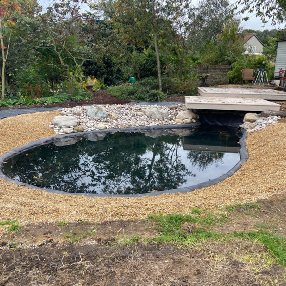oval shaped wildlife pond with shingle banks and overhanging deck at one end