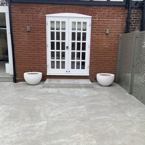 Pristine porcelain patio leading to french windows with a white plant pot either side of the doorstep