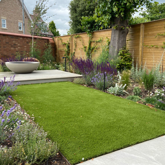 landscaped garden with broad artificial grass walkway bordered by bee friendly planting