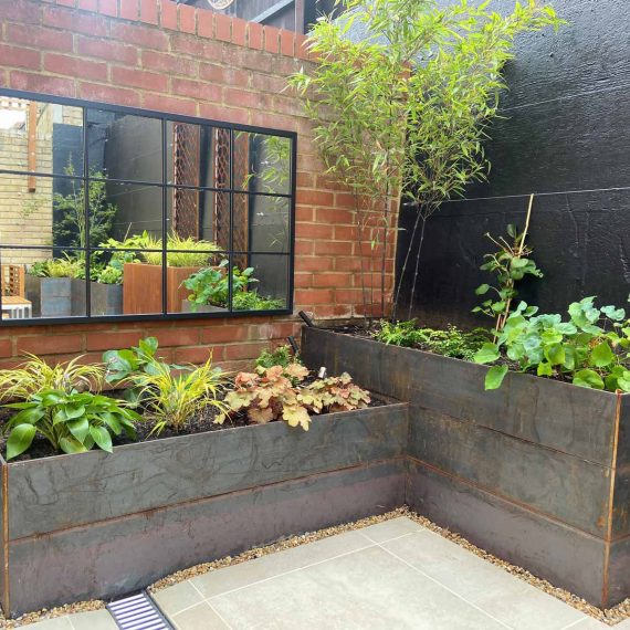 Two dark steel planters at right angles to each other with the rest of the garden reflected in an outdoor mirror